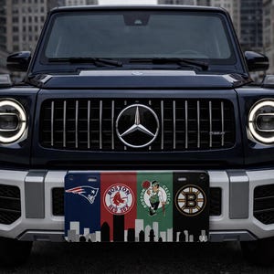 Pode incluir: Um SUV azul escuro com um emblema prateado da Mercedes-Benz na grelha dianteira. O ve&iacute;culo tem uma placa de matr&iacute;cula personalizada com os logotipos dos Patriots, Red Sox, Celtics de Boston e um horizonte de Boston.