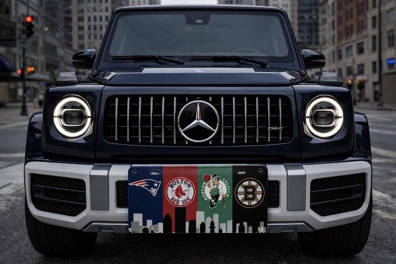 Pode incluir: Um SUV azul escuro com um emblema prateado da Mercedes-Benz na grelha dianteira. O ve&iacute;culo tem uma placa de matr&iacute;cula personalizada com os logotipos dos Patriots, Red Sox, Celtics de Boston e um horizonte de Boston.