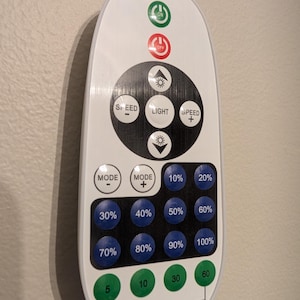 May include: A white remote control with a black circular control pad featuring buttons for light, speed, and mode. It includes blue buttons labeled 10% through 100% for brightness, green timer buttons labeled 5, 10, 30, 60, and red and green power buttons.