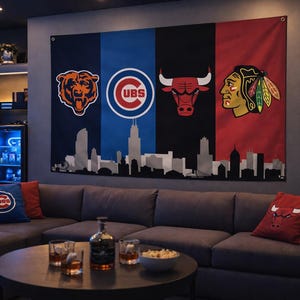 May include: A large wall flag displaying the logos of the Chicago Bears, Cubs, Bulls, and Blackhawks, with a Chicago skyline silhouette. The flag hangs above a grey sectional sofa with matching throw cushions. A round coffee table holds drinks and snacks.