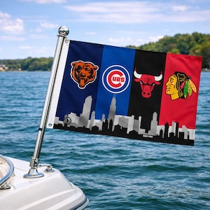 May include: A flag displaying the logos of the Chicago Bears, Cubs, Bulls, and Blackhawks, with a city skyline silhouette. The flag is attached to a boat, set against a backdrop of a lake and trees.