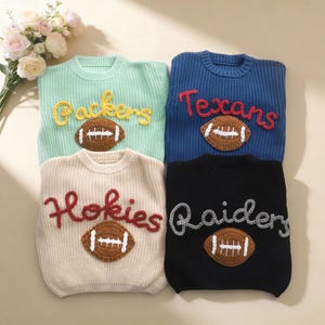 May include: Four knitted sweaters in pastel colors: light green, blue, beige, and black. Each sweater features a team name in a contrasting color and a football applique. The sweaters are arranged on a light-colored surface.