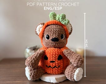 May include: A brown crochet bear wearing an orange pumpkin costume with a green stem on its head. The bear has white inner ears and paw pads. Text reads PUMPKIN BEAR PDF PATTERN CROCHET ENG/ESP. A vertical line indicates a height of 24 cm.