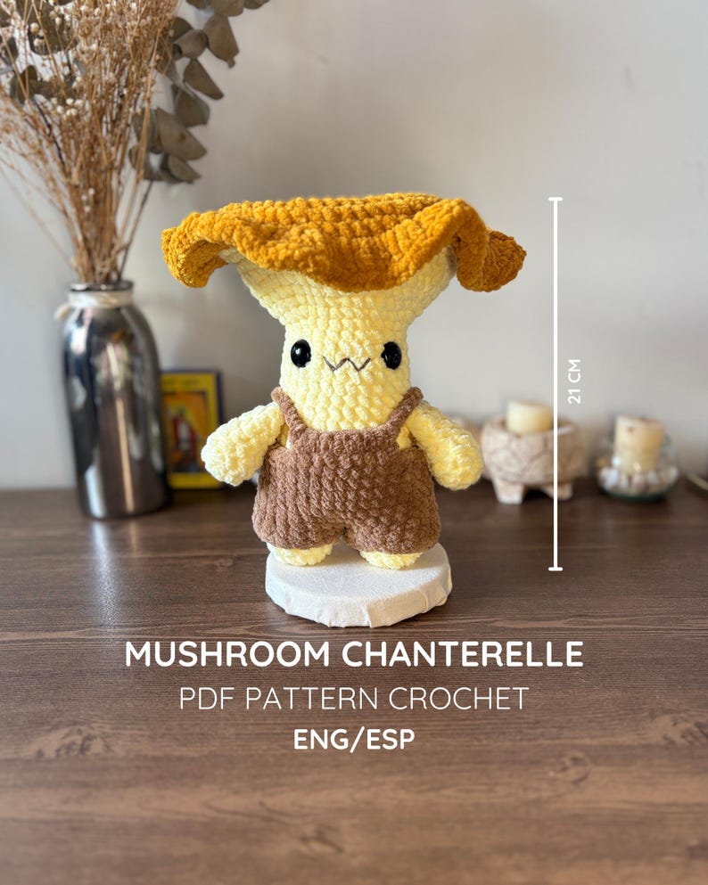 May include: A crochet mushroom doll with a golden-yellow cap and a pale yellow stem, wearing brown overalls. The doll has black bead eyes and a stitched mouth. A vertical line indicates a height of 21 cm. Text reads: MUSHROOM CHANTERELLE PDF PATTERN CROCHET ENG/ESP.