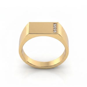 May include: A gold signet ring featuring a flat, rectangular top surface. The right side of the rectangular face is accented with a vertical row of four small, clear, round-cut stones set into the polished gold band.