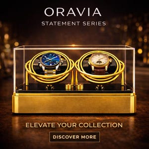 May include: A gold-coloured watch display case with two watches. The case has a clear top and a black base. The watches have gold and silver bands and are displayed on gold-coloured holders. The text "ORAVIA STATEMENT SERIES" and "ELEVATE YOUR COLLECTION" are visible.