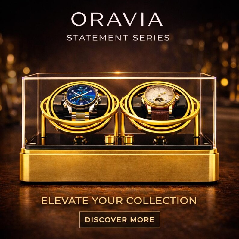 May include: A gold-coloured watch display case with two watches. The case has a clear top and a black base. The watches have gold and silver bands and are displayed on gold-coloured holders. The text "ORAVIA STATEMENT SERIES" and "ELEVATE YOUR COLLECTION" are visible.