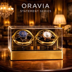 May include: A gold and glass watch display case with two watches. The watches are in a gold-coloured rotating holder. The case has the text "ORAVIA STATEMENT SERIES" on the top.