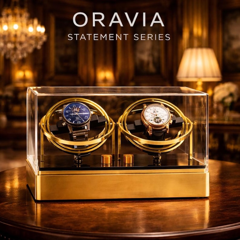 May include: A gold and glass watch display case with two watches. The watches are in a gold-coloured rotating holder. The case has the text "ORAVIA STATEMENT SERIES" on the top.