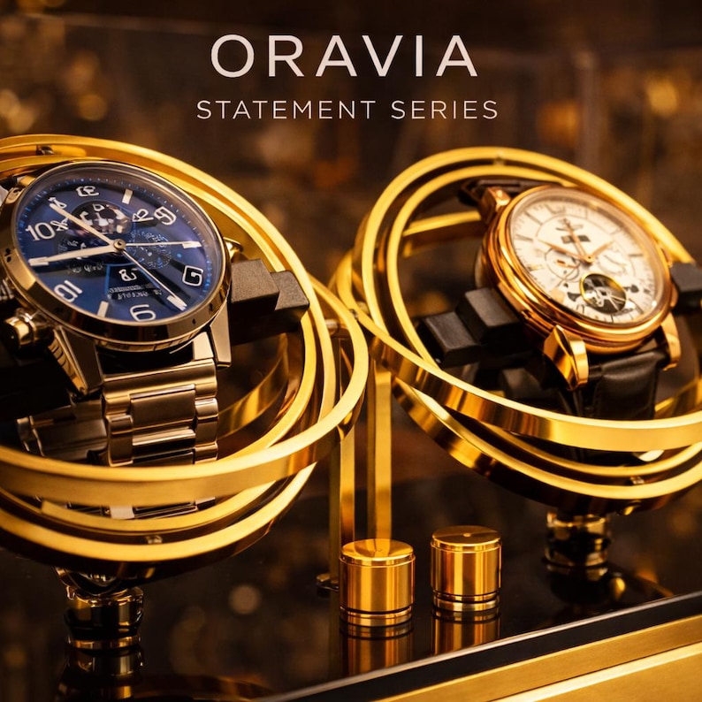 May include: Two gold-toned luxury watches on display. One watch has a blue face, the other a white face. The watches are displayed on gold-coloured stands. The text "ORAVIA STATEMENT SERIES" is at the top.