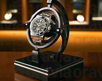 May include: A black and silver watch winder with a stainless steel watch. The watch has a black face and a silver strap. The winder is on a black base with silver trim and a curved black frame.
