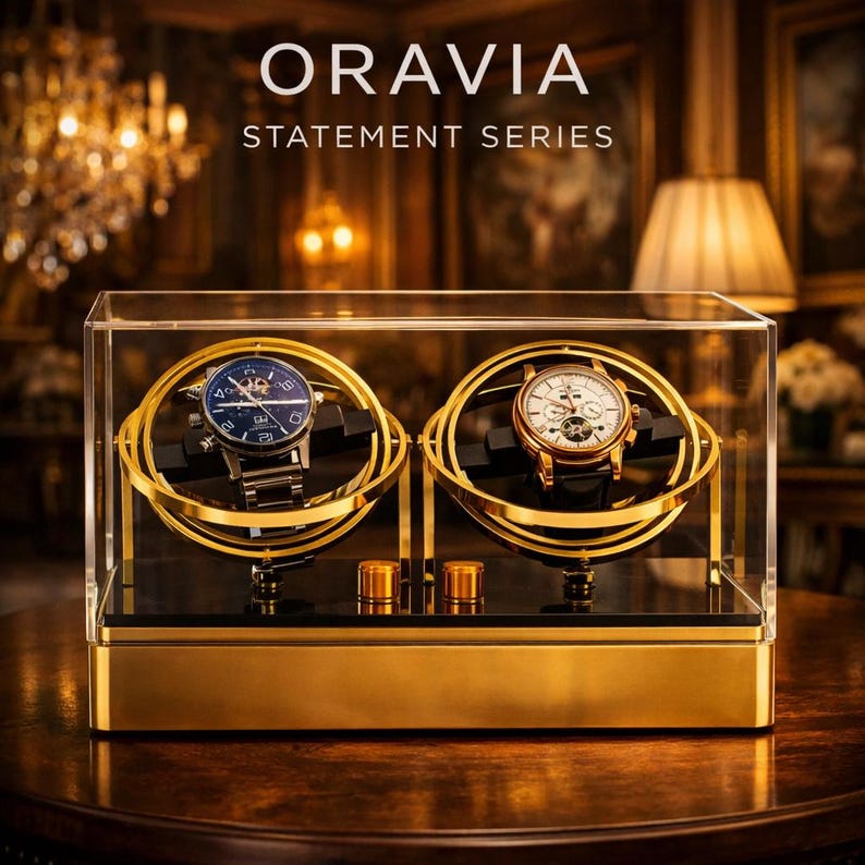 May include: A gold watch display case with two watches. The case is clear with gold detailing and the text "ORAVIA STATEMENT SERIES". The watches have black and gold straps and faces, presented in a luxurious setting.