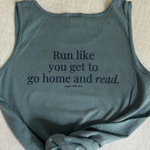 Può includere: Canotta blu turchese con il testo "Run like you get to go home and read." e le parole "pages with olive" in un carattere più piccolo sotto.