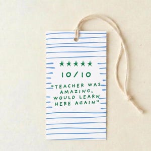 May include: A white rectangular gift tag with blue horizontal lines and a cream-colored string. The tag features green stars, the number 10/10, and the text "TEACHER WAS AMAZING, WOULD LEARN HERE AGAIN."