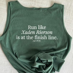 Può includere: Canotta verde con testo bianco che recita "Run like Xaden Riorson is at the finish line." Il testo è centrato sul retro della canotta.