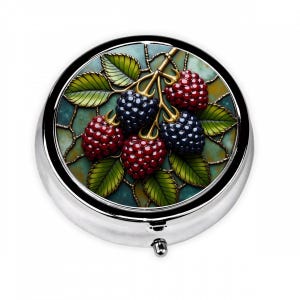 May include: A silver-toned, round pill box with a detailed design of blackberries and leaves. The berries are red and dark blue, with green leaves and a gold-colored stem. The background is a mosaic of teal and gold.