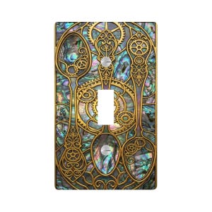 May include: A decorative light switch cover with a steampunk design. The cover features three spoon-shaped elements with intricate gear details, set against an iridescent background. The design is framed in gold, with a white switch in the center.