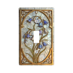May include: A rectangular light switch cover plate featuring a central oval frame with a gold-toned border. The design displays a mosaic pattern of blue and white bell-shaped flowers with green stems against a background of iridescent white tiles.