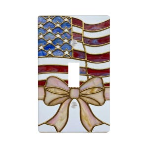 May include: A decorative light switch cover featuring a stained glass design of the American flag with red and white stripes, blue stars, and a pink bow. The switch cover is rectangular and has a single toggle switch opening.