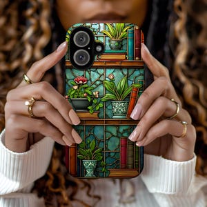 iPhone case with an intricate stained glass-style design featuring bookshelves adorned with potted plants, blooming flowers, and colorful books. The background showcases a rich teal mosaic pattern, creating a warm, vintage-inspired botanical library look.