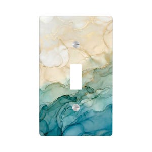 May include: A decorative light switch cover with a marbled design. The cover features a blend of colors, including gold, teal, and blue, creating an abstract, flowing pattern. It has a single toggle switch and two silver screws.