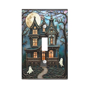 May include: A decorative light switch cover featuring a spooky haunted house design. The artwork includes a full moon, silhouetted trees, and two white ghosts. The house is dark blue with gold accents, perfect for Halloween.