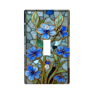 May include: A decorative light switch cover featuring a stained-glass design. The cover showcases vibrant blue flowers with gold outlines against a mosaic background of blues and greens. The switch is white.