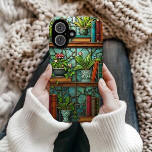 May include: A phone case featuring a colorful design of a bookshelf with potted plants and books. The case has a teal background with a stained glass effect. The plants include a red rose and various green plants.