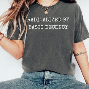 May include: A dark gray t-shirt with the text "Radicalized by Basic Decency" printed in white on the front.