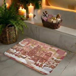May include: A rectangular bath mat featuring a printed patchwork design of a winter village scene with houses, trees, and a horse-drawn carriage in shades of pink, brown, and white, placed on a marble floor in a bathroom setting.