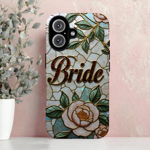May include: A phone case with a stained-glass effect, displaying the word "Bride" in gold script. The design includes pink roses, green leaves, and gold detailing. The phone's camera is visible at the top. The case has a floral pattern.