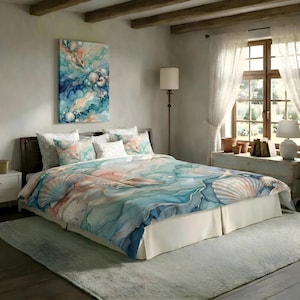 May include: A bedding set featuring a watercolor-style print of seashells and starfish in shades of blue, teal, and soft peach. The set includes a duvet cover and matching pillow shams, all displaying a fluid, ocean-inspired pattern.