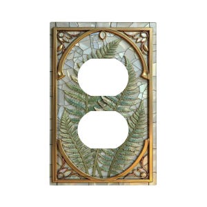 May include: Decorative light switch cover with a gold-colored frame and a mosaic background. The design features a fern motif in shades of green and gold, with two circular openings for outlets.