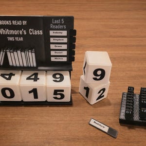 May include: A black and white classroom reading tracker with the text "BOOKS READ BY Mrs. Whitmore's Class THIS YEAR". It includes number blocks, a name tag, and a section for the last five readers.