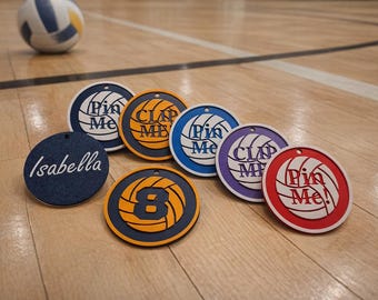 May include: A collection of round volleyball-themed tags in various colors, including blue, orange, purple, and red, with white text. One tag has the name "Isabella". A volleyball is in the background. The tags say "Pin Me" and "Clap Me".