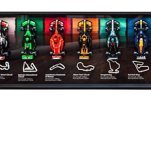 Peut inclure: Une vitrine encadrée de voitures de course miniatures de Formule 1, chacune représentant un circuit différent. Les voitures sont peintes aux couleurs des équipes qui courent sur chaque circuit. Les circuits sont listés sous chaque voiture, y compris le nom du circuit et la longueur du circuit en kilomètres.