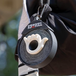 May include: A black and white Rip N Roll tape dispenser with a white hand shaped like a hang loose gesture. The dispenser is attached to a black bag.