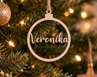 Könnte beinhalten: Ein kreisförmiger Weihnachtsbaumanhänger aus hellem Holz mit dem Namen Veronika, der in einer Schreibschrift ausgeschnitten ist. Der Anhänger hat eine kleine Öse an der Oberseite und ist an einem dünnen Stück Naturkordel befestigt.