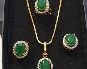 May include: A gold-toned jewelry set featuring a ring, pendant necklace, and earrings. Each piece has a large, round, green gemstone surrounded by a halo of smaller, clear stones. The set is displayed in a black box.