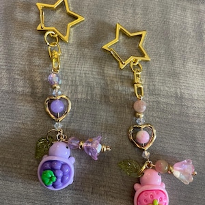 May include: Two keychains with gold star clasps. One keychain features a purple turtle with a green flower, the other a pink strawberry turtle with a green flower. Both have heart-shaped charms and beaded accents.