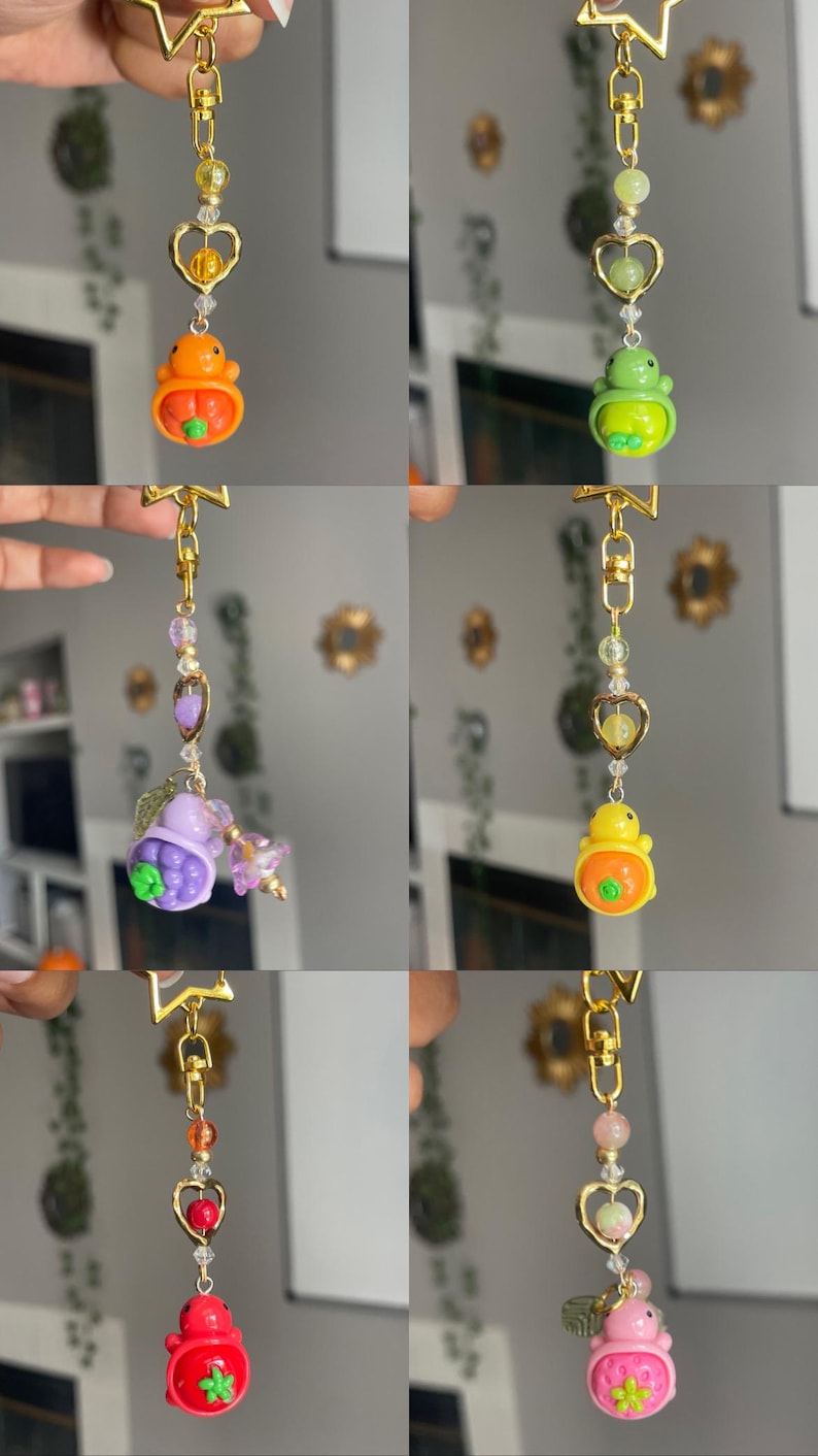 May include: A collection of six keychains with gold-colored hardware. Each keychain features a charm with a unique design, including a pumpkin, a frog, a berry, a strawberry, and a pink strawberry. The keychains are adorned with beads and heart-shaped accents.