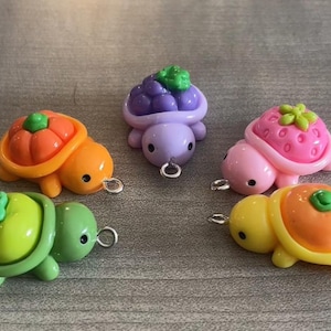 May include: A collection of colorful turtle charms, each with a different fruit-themed shell. The charms include a pumpkin, grapes, strawberry, and orange. Each turtle has a small silver loop for attaching to jewelry or other crafts.