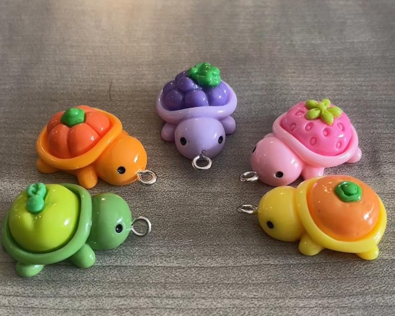 May include: A collection of colorful turtle charms, each with a different fruit-themed shell. The charms include a pumpkin, grapes, strawberry, and orange. Each turtle has a small silver loop for attaching to jewelry or other crafts.