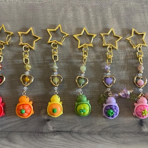 May include: A collection of seven colorful keychains. Each keychain features a gold star-shaped clasp, a beaded chain, a heart-shaped charm, and a turtle-shaped pendant in various colors like red, orange, yellow, green, purple, and pink.