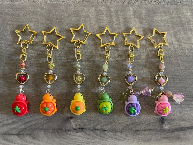 May include: A collection of seven colorful keychains. Each keychain features a gold star-shaped clasp, a beaded chain, a heart-shaped charm, and a turtle-shaped pendant in various colors like red, orange, yellow, green, purple, and pink.