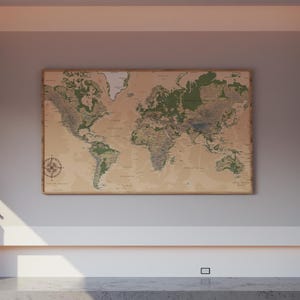 May include: A framed world map with a vintage aesthetic. The map features detailed geographical information, with green-colored landmasses and a compass rose in the lower left corner. The map is mounted on a light-colored wall.