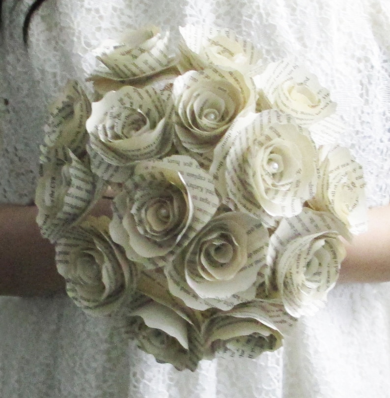 May include: A bouquet of paper roses crafted from book pages. The roses are white and have a delicate, vintage appearance. Each rose features a small pearl at its centre.