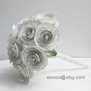 May include: A bouquet of white paper roses made from book pages, with pearl accents, and a white lace ribbon around the stems.
