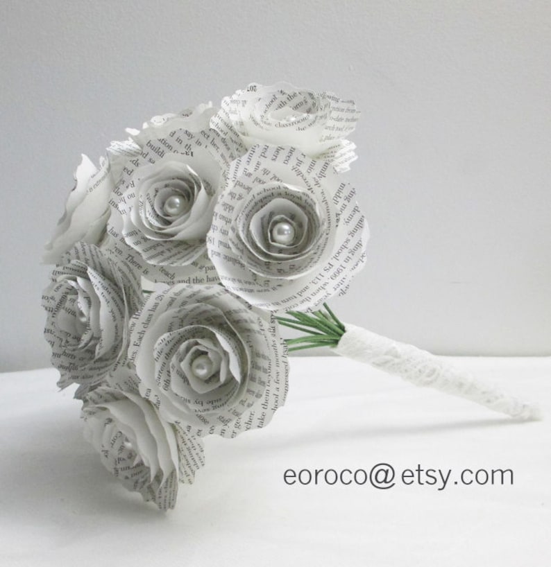 May include: A bouquet of white paper roses made from book pages, with pearl accents, and a white lace ribbon around the stems.