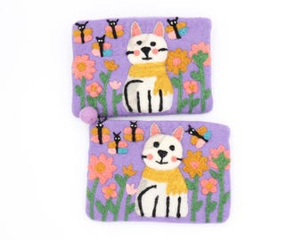 Può includere: Due pochette in feltro lavanda con ricami di gatti. Ogni pochette presenta un gatto bianco con una sciarpa gialla, circondato da fiori e farfalle. Una pochette ha un piccolo pompon viola attaccato.